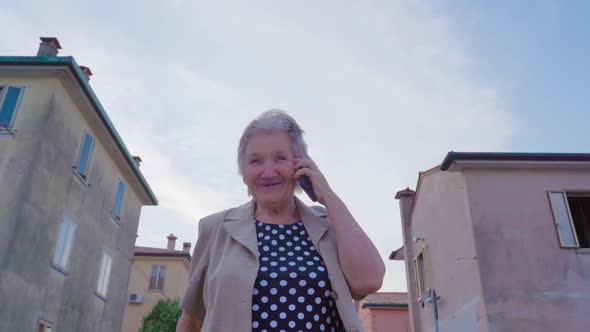 Elderly Woman Talks on Phone Standing on Street in Chioggia