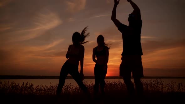 Silhouettes of Friends Dancing Rejoicing in Field at Sunrise