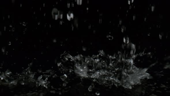 Pouring water on black surface against black background. Slow Motion.