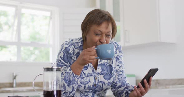 Happy african american senior woman enjoying drinking cup of coffee and using smartphone