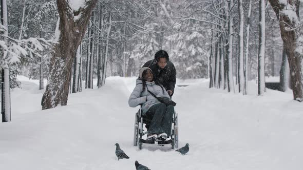 Young Couple of Asian Guy and His Black Girlfriend in the Wheelchair Walking in Winter Forest