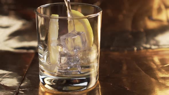 Sparkling water is poured into a glass with lemon and ice cubes. 