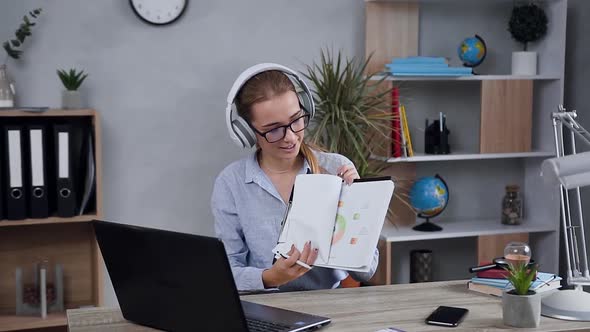 Woman in Headphones with Financial Reports in Hands which Having Videocall with Client