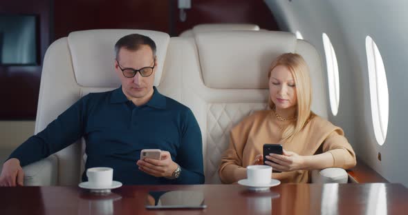 Mature Couple Drinking Coffee and Using Smartphone Flying on Private Jet