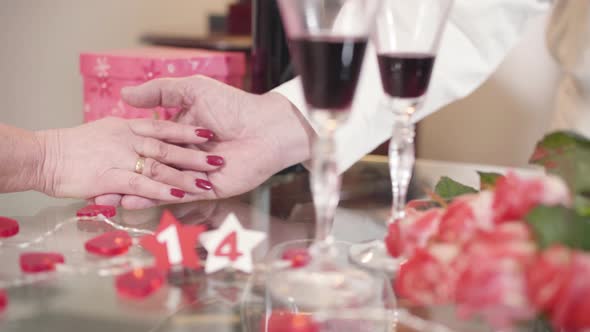 Close-up of Male Mature Caucasian Hand Taking and Stroking Wife's Palm. Blurred Bouquet Lying on the