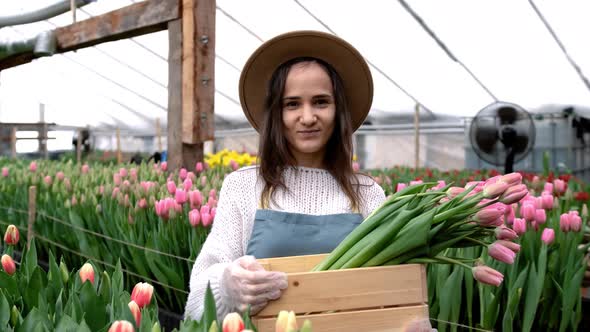 A Young Farmer Girl in a Hat Holds a Wooden Box with Bouquets of Tulips in Her Hands