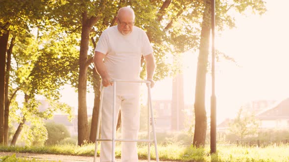 Disabled old man is walking with a walker. Handicapped patient in the park.