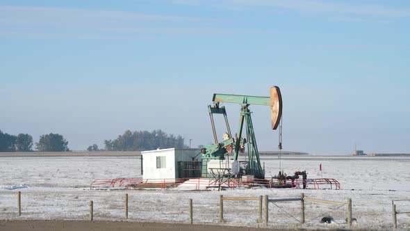 Oil Pumpjack Operating in a Snowy Field on a Foggy Morning