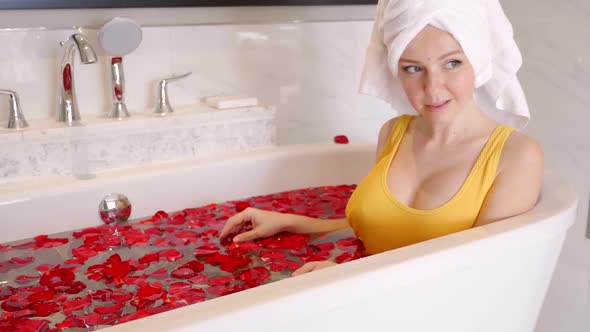 Attractive Young Woman with Towel on Head Taking a Bath Full of Rose Petals