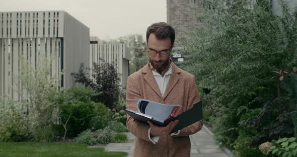 Cheerful Bearded Man in Glasses Holding Paper Folder While Reading Finance Documents. Stylish