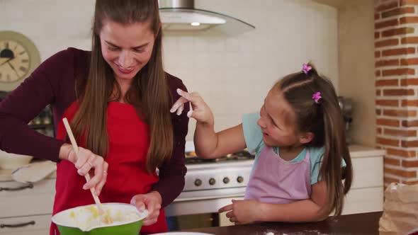 Caucasian mother and daughter wearing aprons having fun while baking together in the kitchen at home