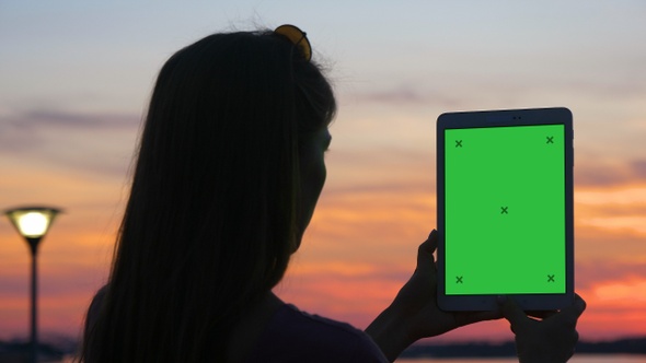 Woman taking photos at sunset using a tablet.