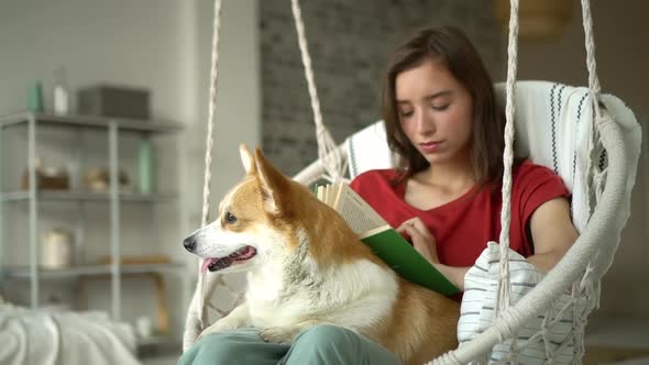 Young American Woman is Reading Book and Spending Day with Dog in Apartment Room Avki