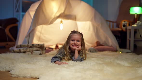 Wide Shot Portrait of Charming Little Caucasian Girl Smiling Looking at Camera Lying at Tent in