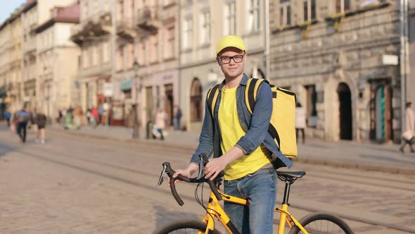 Portrait of a Happy Delivery Man Who is Sitting on a Bicycle and Looking at the Camera