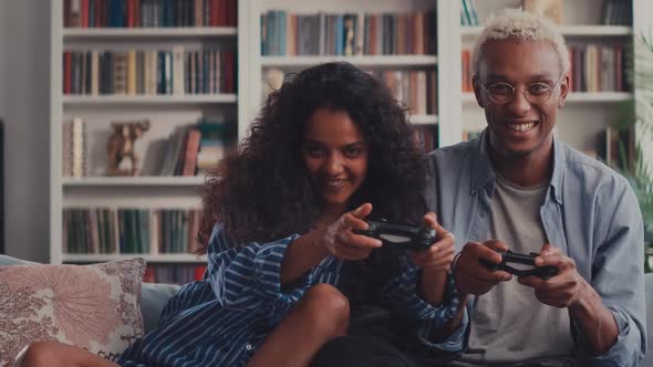 Happy Mixed Race Couple Sitting on Sofa Playing Video Games Using Controllers