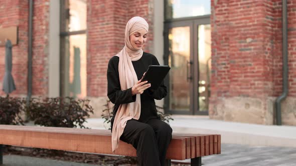 Cheerful Young Islamic Businesswoman Working on Tablet While Sitting Near Her Office