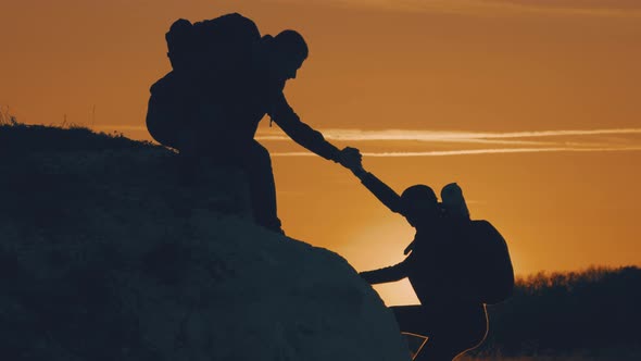 Silhouette of Helping Hand Between Two Climber, Two Hikers on Top of the Mountain, a Man Helps