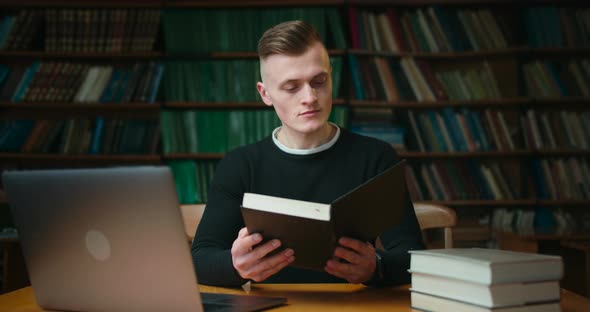 A Young Man Is Looking in the Book in the Reading Room of the Library. Education in the Library. 