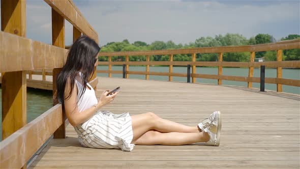 Cute Woman Is Reading Text Message on Mobile Phone While Sitting in the Park.