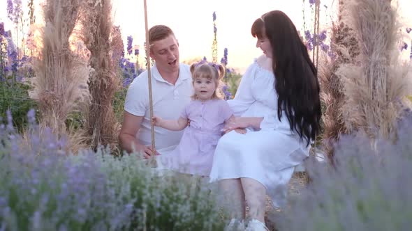 Beautiful Young Family Mom and Dad with Daughter in Nature Happy Family on a Swing