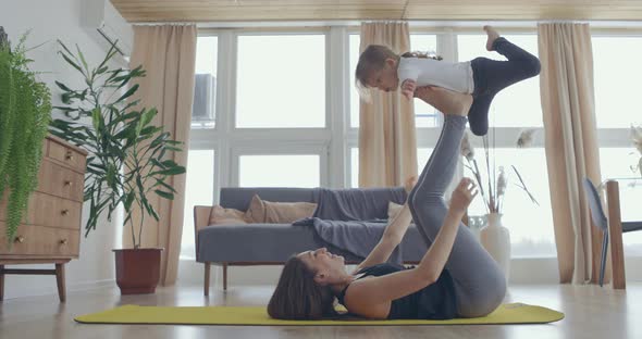 Happy Beautiful Family Healthy Young Mom Lifting Cute Little Child Daughter Up Playing Plane on Wall