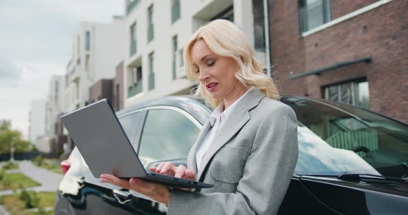 Woman in Formal Clothes Standing in front of the Black Car, Using Laptop