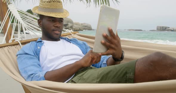 Front view of African american man using digital tablet on the beach 4k