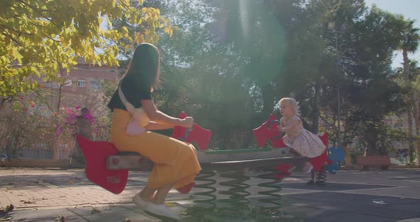 Attractive Happy Young Mother with Baby Girl in Playground Riding on a Swing