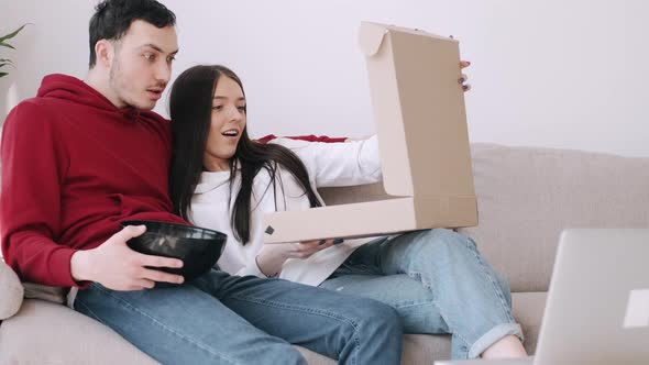 Boy and Girl in Hoodies Are Surprised Having a Takeaway Pizza and Watching Films on Laptop