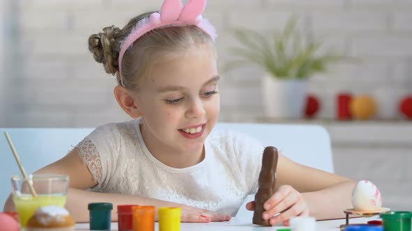 Adorable Girl Playing With Chocolate Bunny and Smiling Into Camera, Childhood