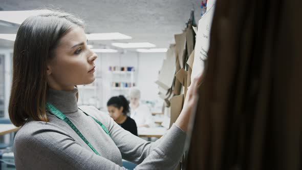 Young Woman Fashion Designer or Tailor of Sewing Workshop is Talking While Choosing Pattern Hanging