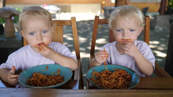 Two Caucasian Toddlers Develop Their Motor Skills By Eating Pasta with Hands
