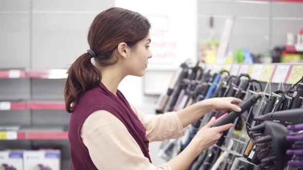 Attractive Girl in Her 20's Choosing Flat Iron From a Variety in Appliance Store