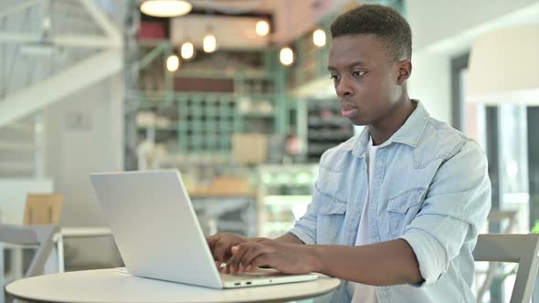 Cheerful African Man Working on Laptop in Cafe