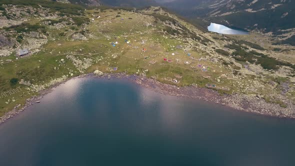 Tilting shot revealing tents at the base of a valley with mountains in the background.