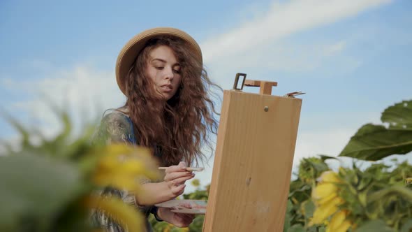 Smiling Female Artist Painting Among Sunflowers on Bright Sky View