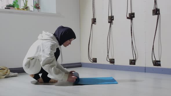 A Young Woman in Hijab Picks Up the Yoga Mat From the Floor