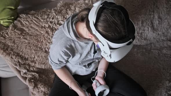 Young Woman Sitting on Sofa Playing Game Using VR Helmet Indoor at Home