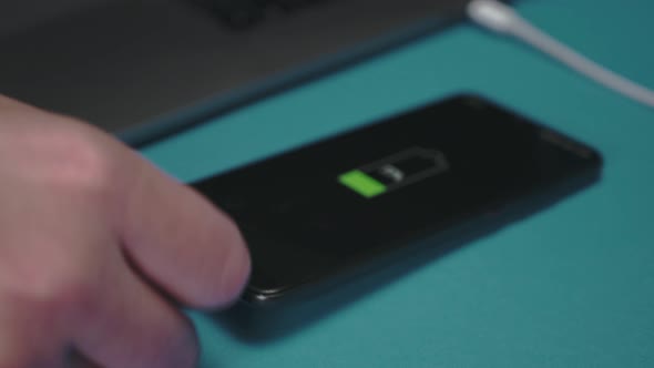A hand inserts the usb-c cord into the smartphone and puts it next to the laptop to charge