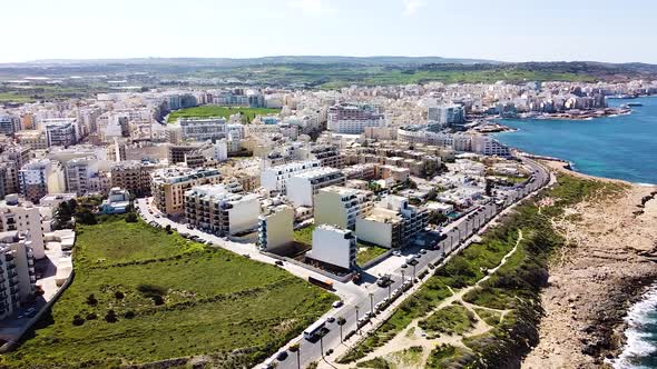 Malta's town situated on rocky coastline with beautiful buildings and green meadows, aerial view