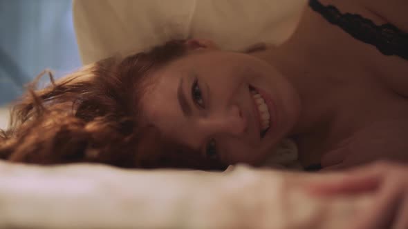 Pretty Young Woman with Red Long Hair Lie Down in Bed and Smile. Leisure of Cute Girl