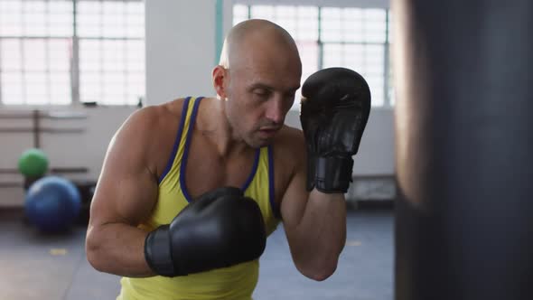 Caucasian male trainer wearing boxing gloves training with punching bag at the gym