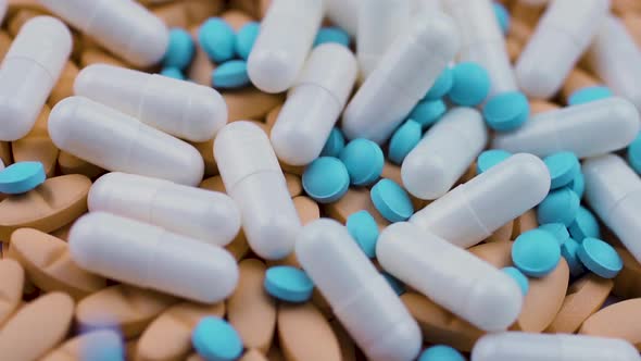 Small Blue Pills Fall on White Capsules with Antibiotic and Orange Vitamins.