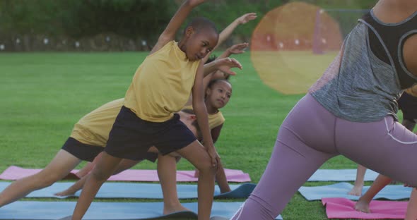 Mixed race female teacher showing diverse group of schoolchildren yoga stretching exercises outdoors