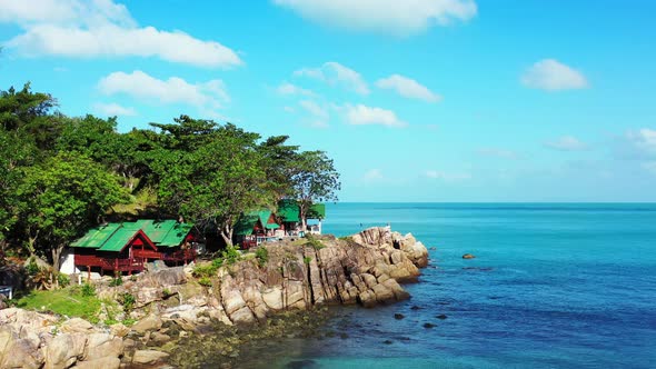 Beach cabins over rocky coastline of tropical island with green vegetation, blue turquoise lagoon re