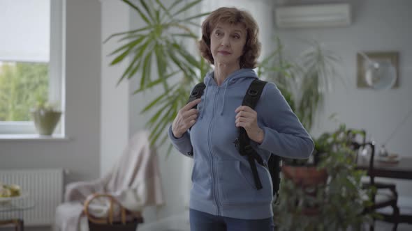 Mature Happy Woman in Blue Hoody Fixing Black Comfortable Backpack at Her Back