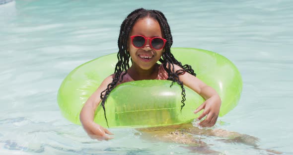 Happy african american girl wearing sunglasses swimming with inflatable ring