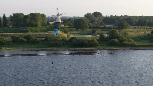 Beautiful Cinematic Aerial Drone Shot of Kitesurfing on a River Past an Old Windmill in Rural Nether