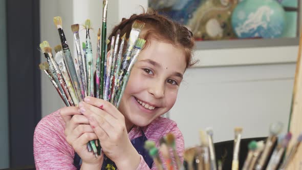 Cute Happy Girl Smiling To the Camera Holding Bunch of Paintbrushes